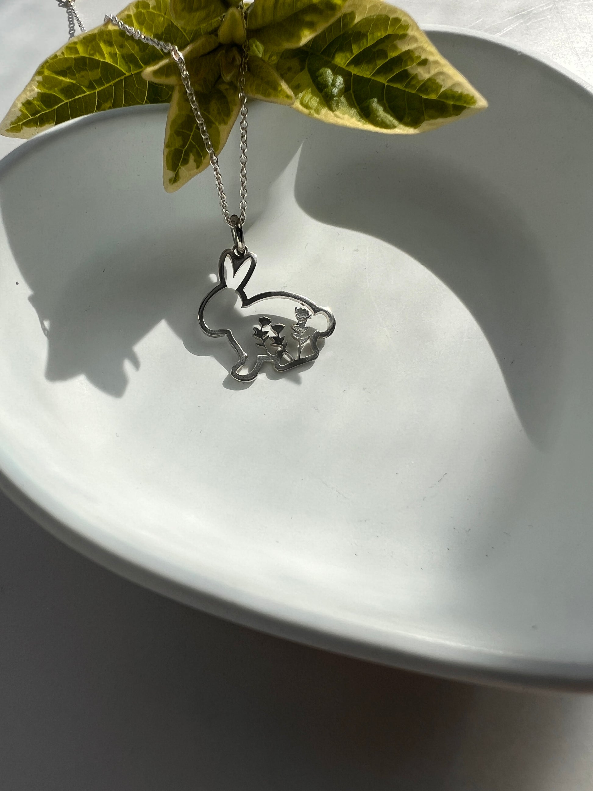 Silver necklace with a pendant on a white dish next to a green leaf